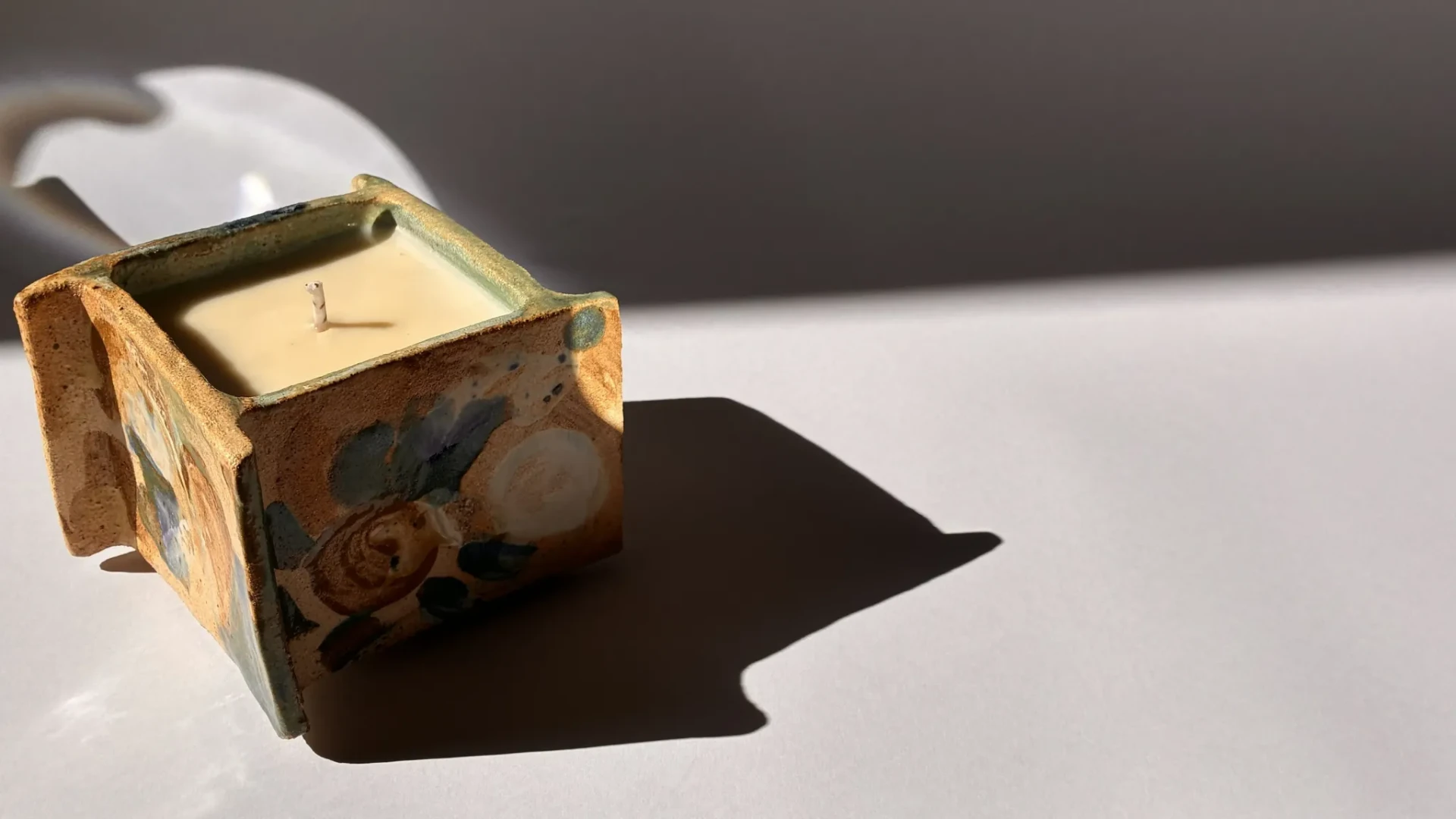 Handmade La Fille ceramic candle in sunlight, casting a long shadow.
